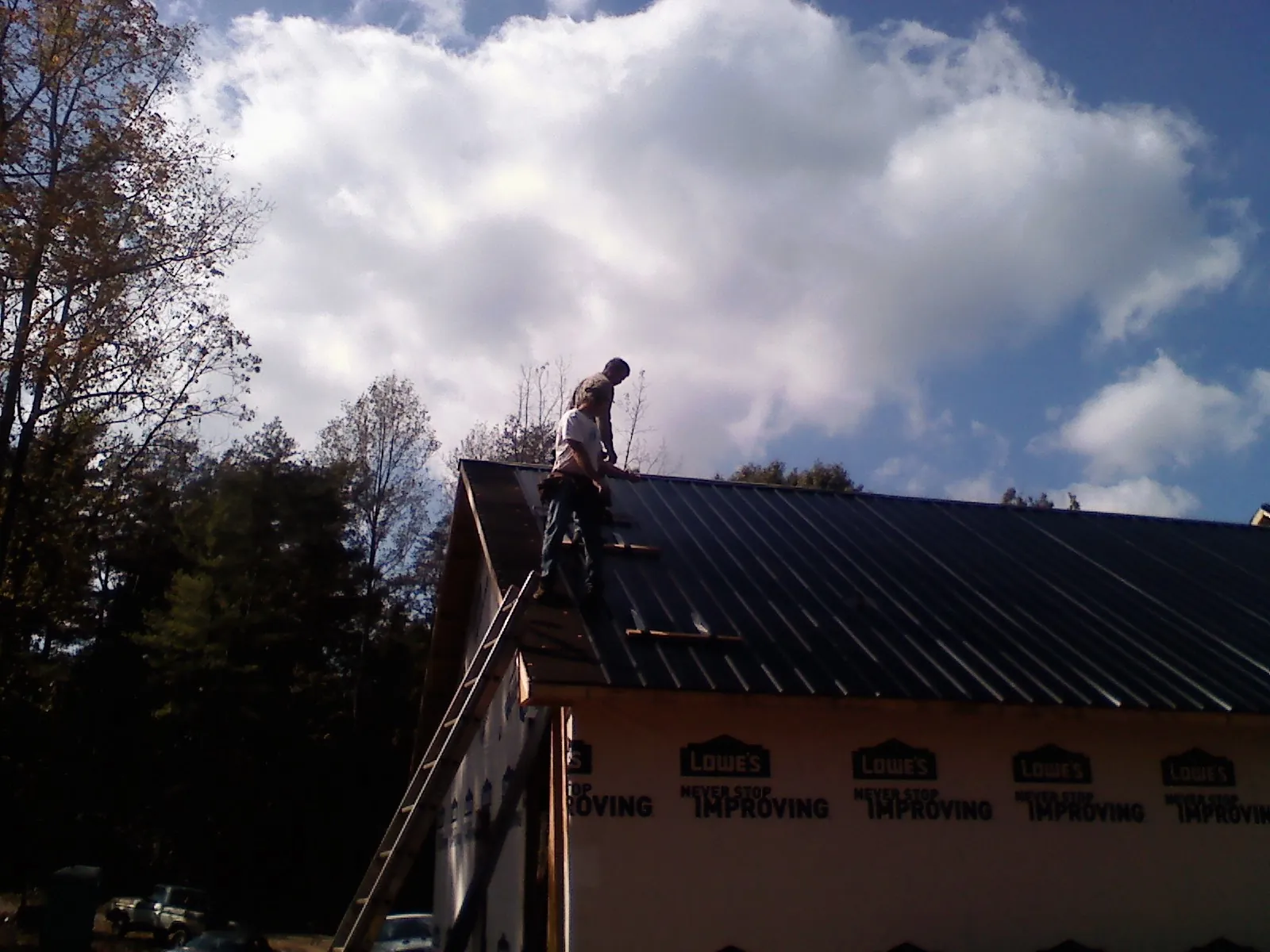 Roofer fastening dark metal panels high against a cloudy sky, from a Roof Inspection job in Portsmouth